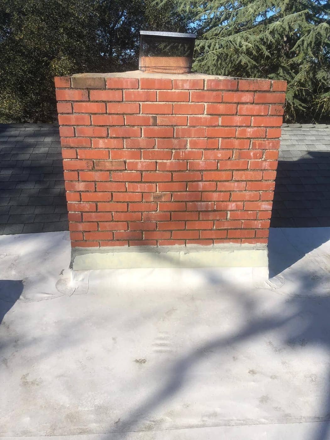 A red brick chimney on a flat roof, with metal flashing along its base.