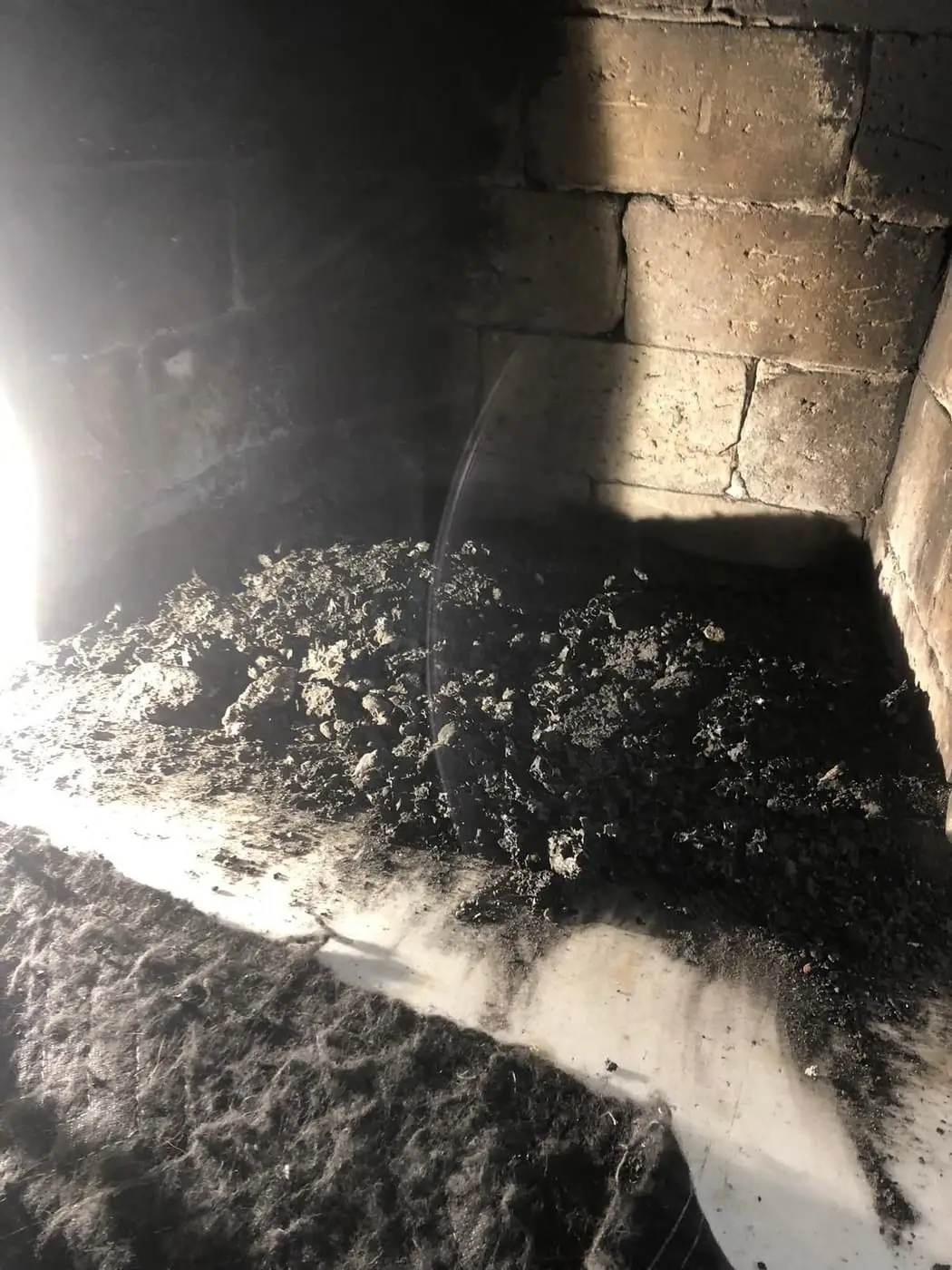 A pile of soot and debris on the floor of a fireplace, lit by a work light.