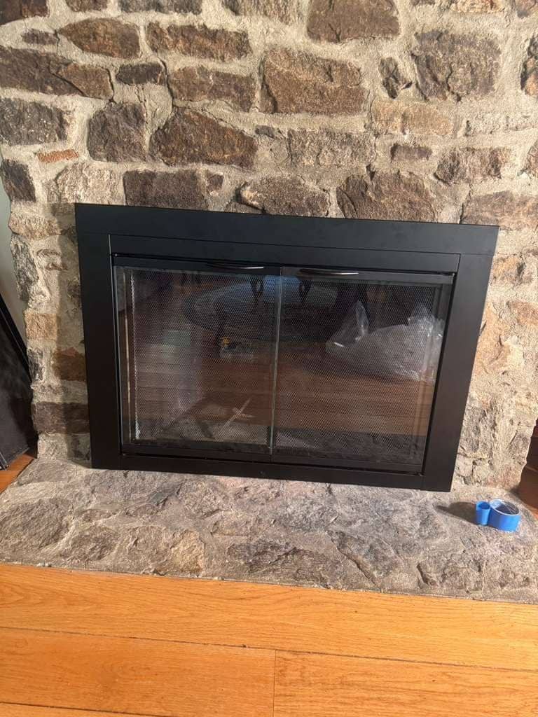 A black glass fireplace door set into a fieldstone fireplace, with a stone hearth below it.