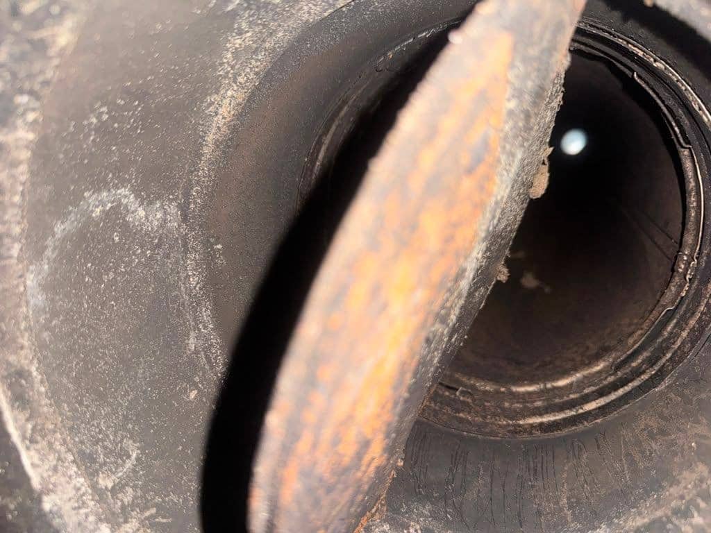 Looking into a round metal flue past a rusted damper plate.