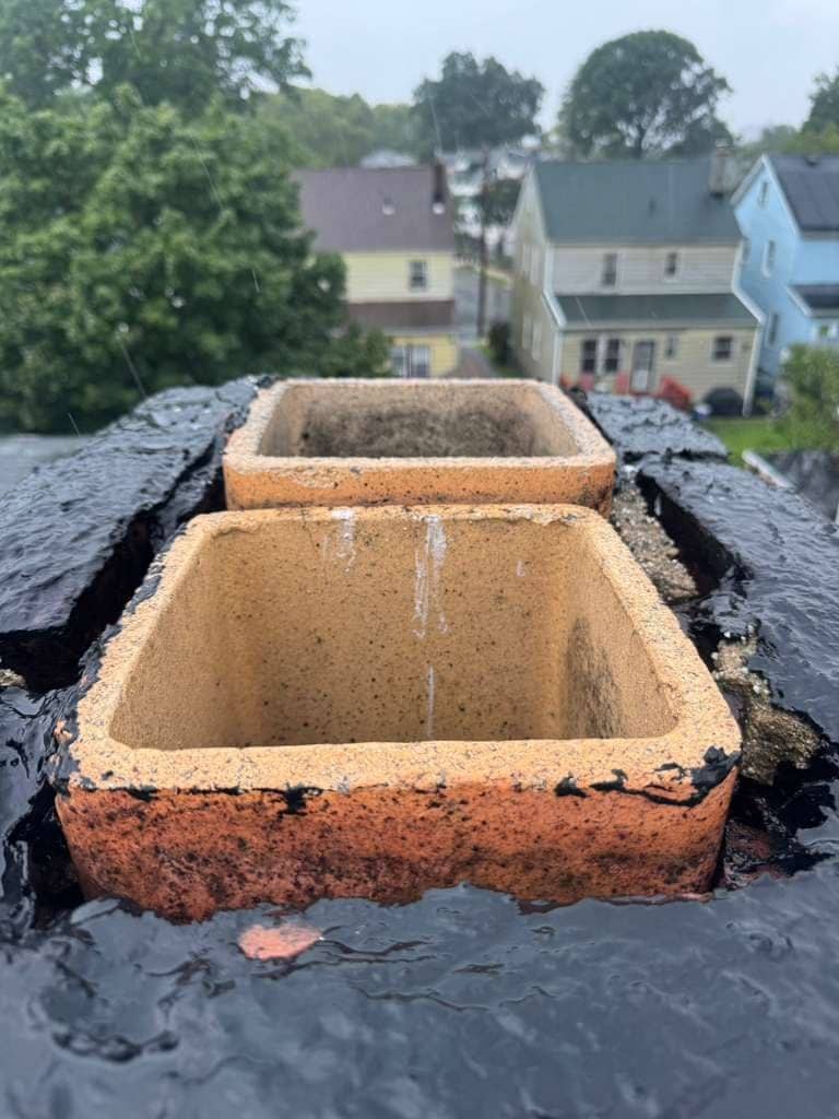Two clay flue tiles rising from a chimney top covered in a fresh black coating, wet from rain.